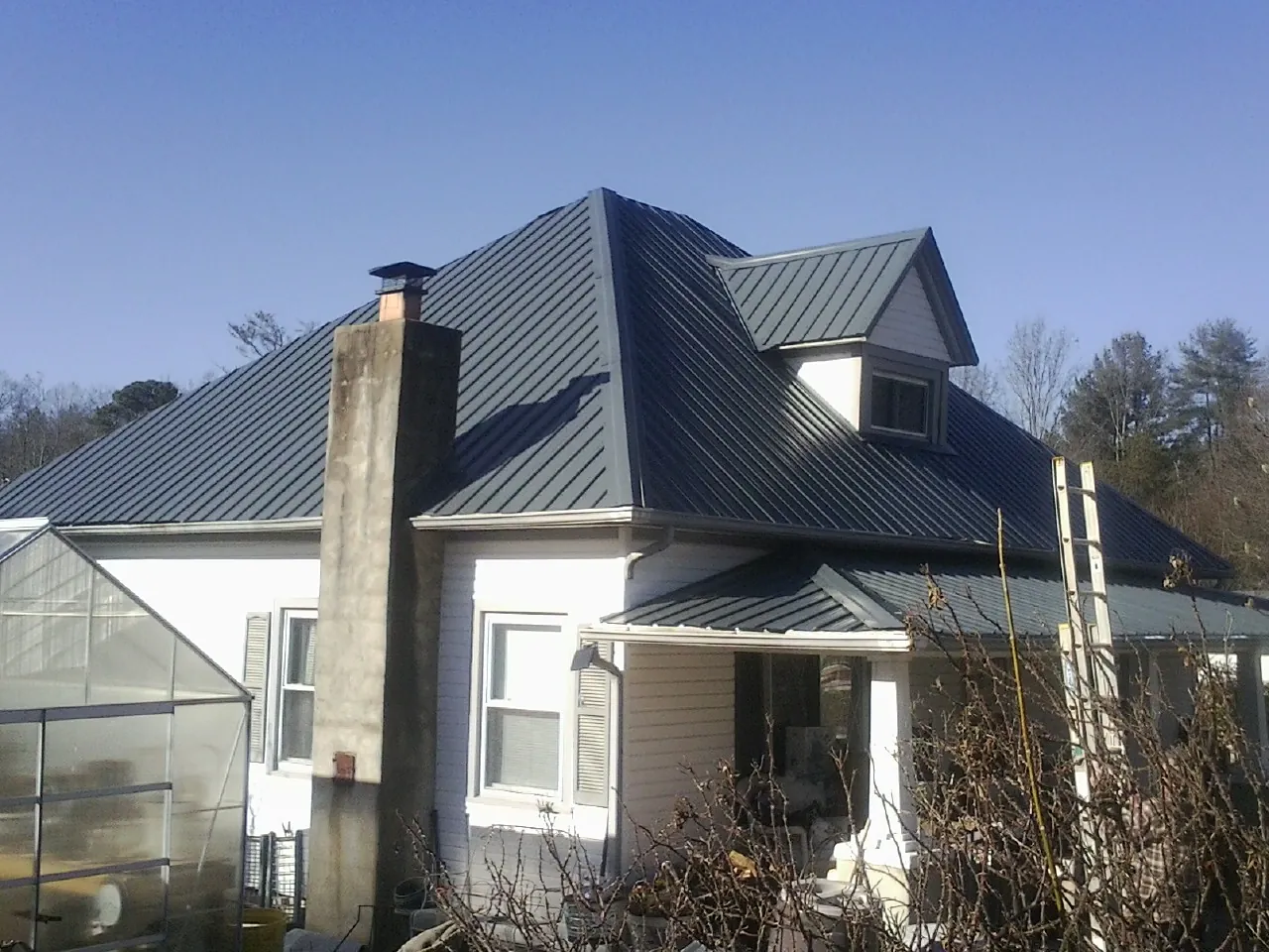 Dark blue standing seam metal roof on a white farmhouse with dormer — Slate & Tile Roof Repair by Roofing Brothers in Guilderland