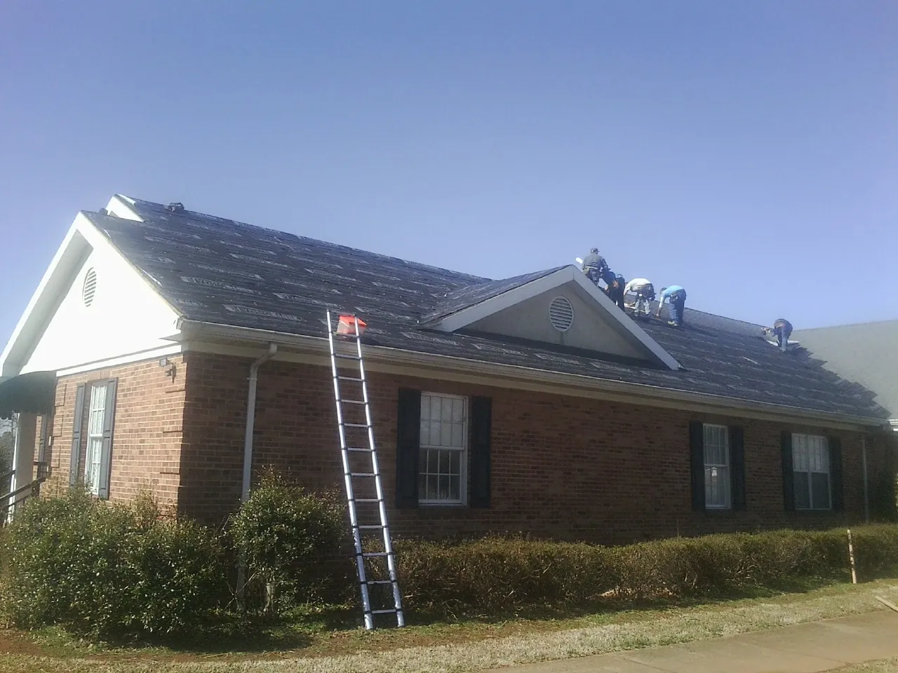 Crew tearing shingles off a brick ranch roof with a ladder set — Metal Roof Repair work by our crew in Guilderland