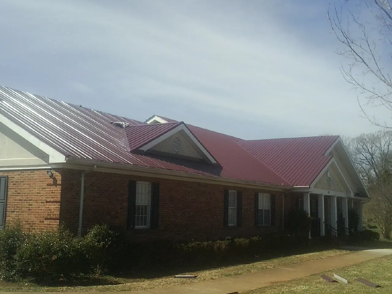 Red metal roof with gabled entries on a long brick building, from a Hail Damage Roof Repair job in Guilderland