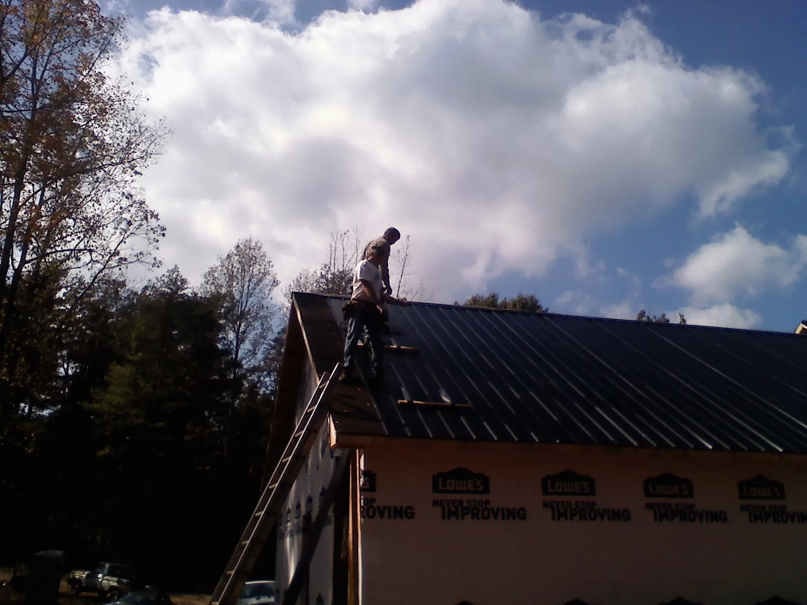 Roofer fastening dark metal panels high against a cloudy sky, from a Roof Inspection job in Guilderland