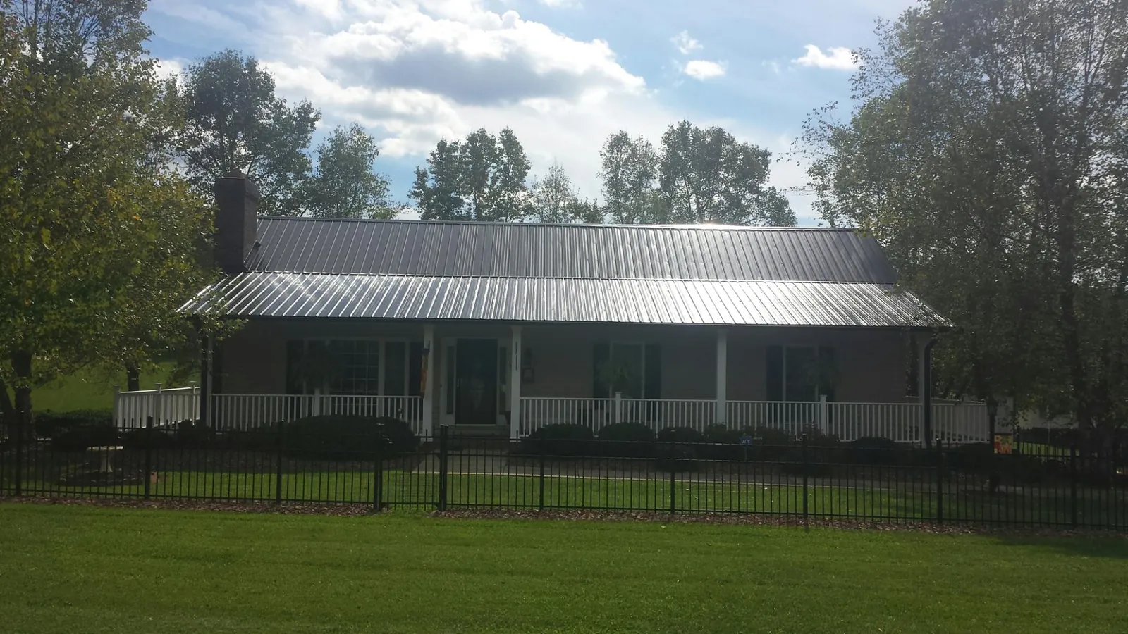 Gray metal roof on a brick ranch with a full width front porch — Gutter Guard Installation work by our crew in Guilderland