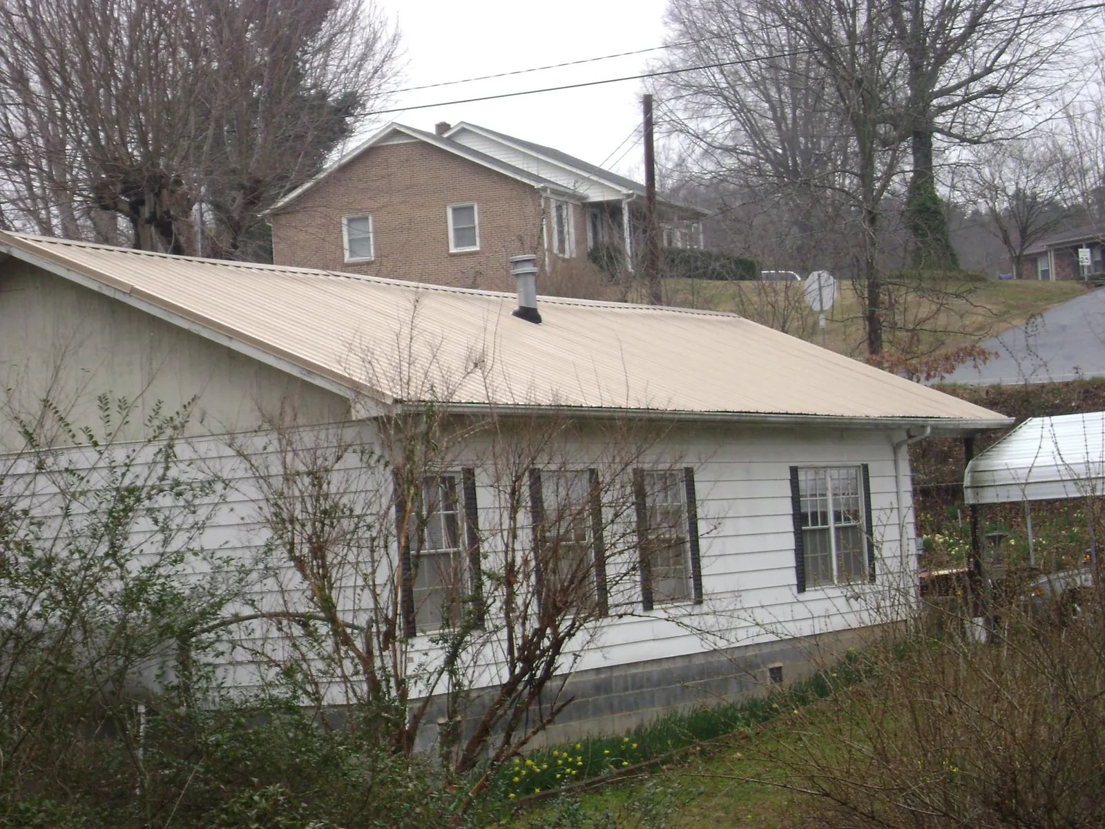 Tan metal roof on a white sided house set into a hillside — Commercial Roofing by Roofing Brothers in Guilderland