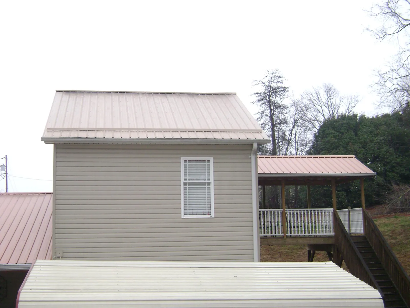 Tan metal roofs on a two story addition and attached porch, from a Roof Replacement job in Guilderland