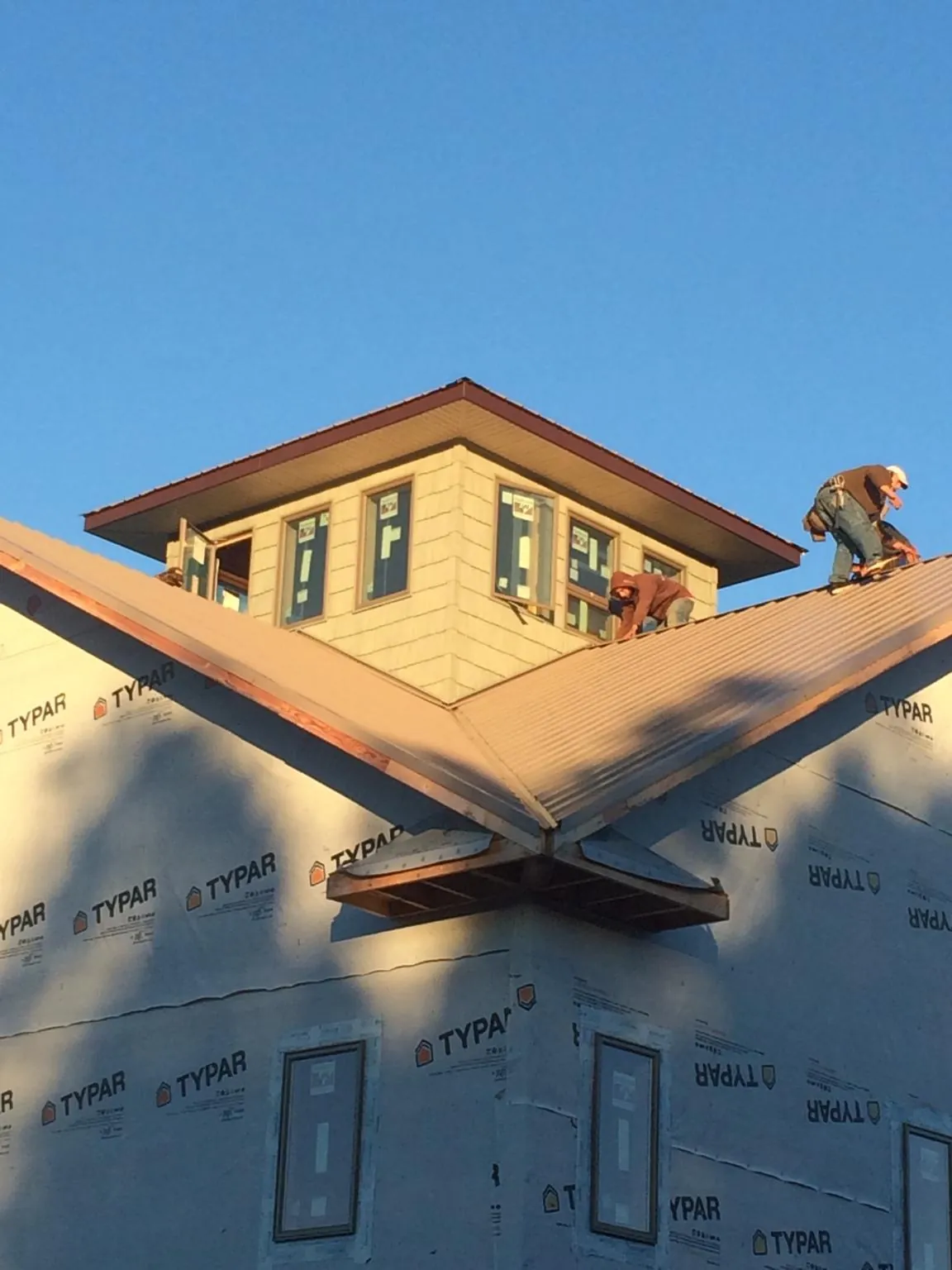 Roofers working around a rooftop cupola on a new metal roof at sunset — Roof Waterproofing in Guilderland by Roofing Brothers